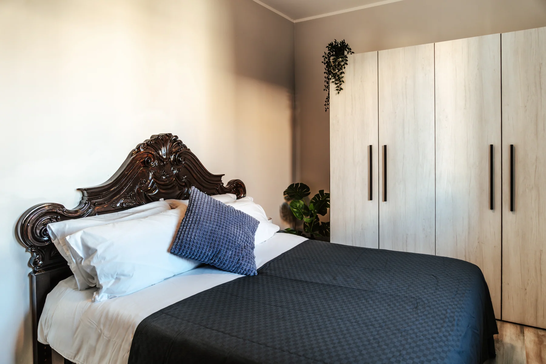 Blu: double bed with a carved wooden headboard and a light-coloured wardrobe